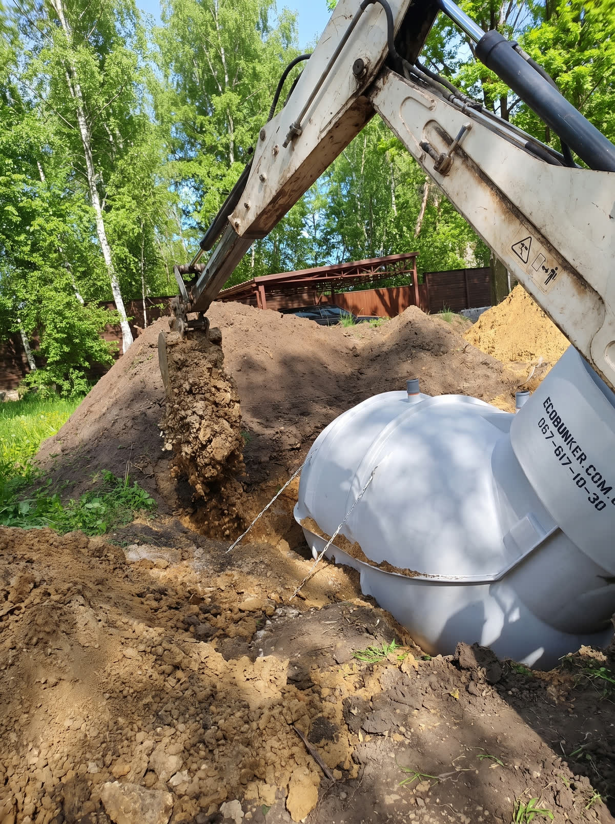 Ківш екскаватора висипає ґрунт поруч із корпусом, видно ланцюг кріплення